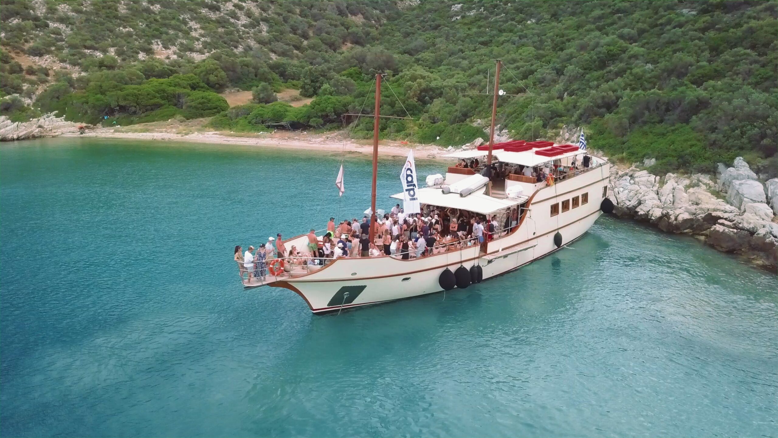 Vue aérienne d'un bateau de loisir avec des gens dessus, dans une crique turquoise,