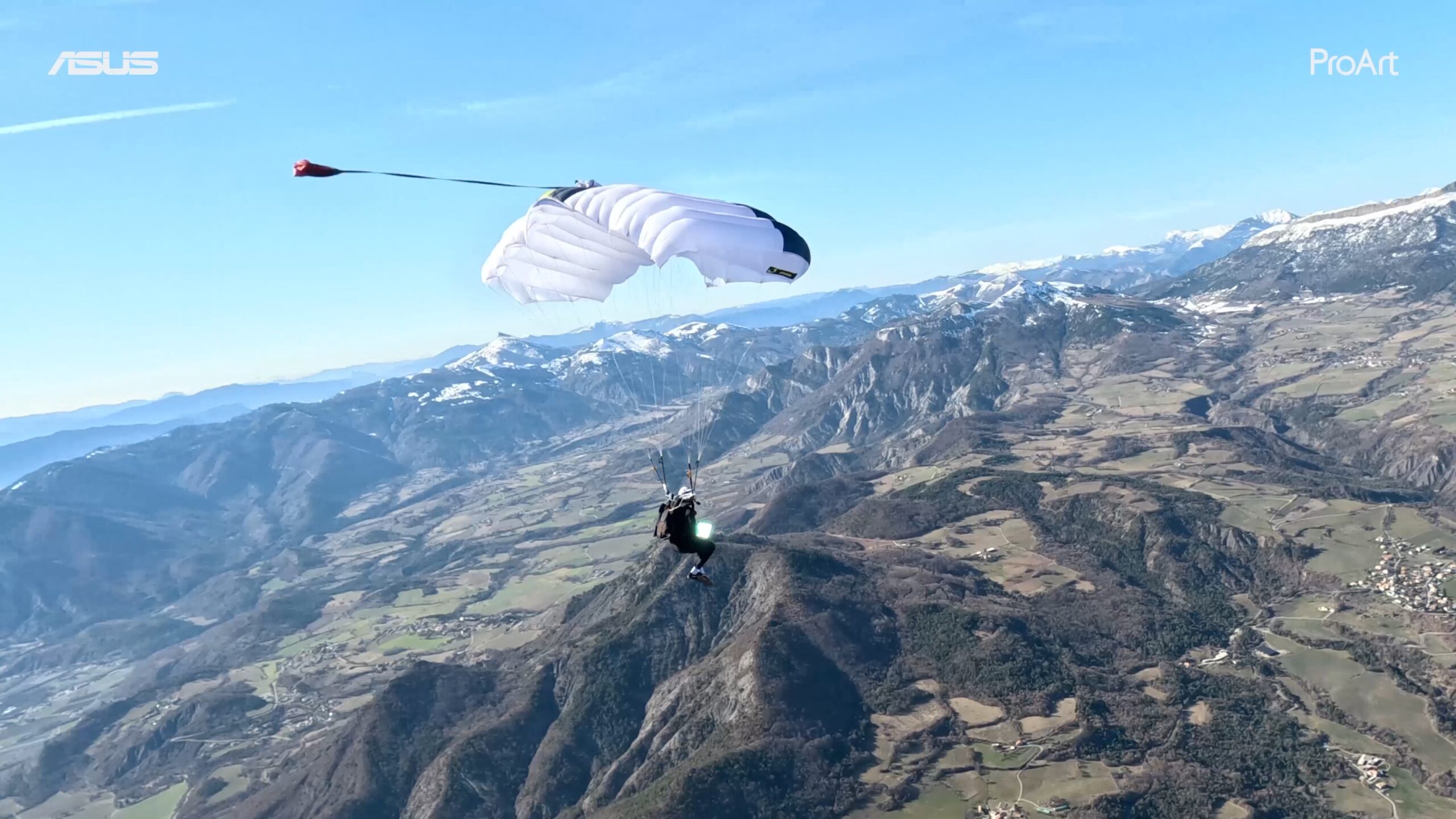 un homme avec un ordinateur, volant en parachute, les montagnes et le ciel derrière lui